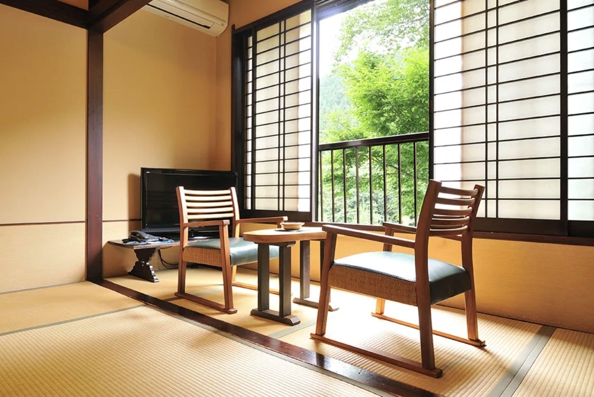 Une pièce de style japonais traditionnel, avec un sol recouvert de tatamis, une table basse, deux chaises en bois et un téléviseur.