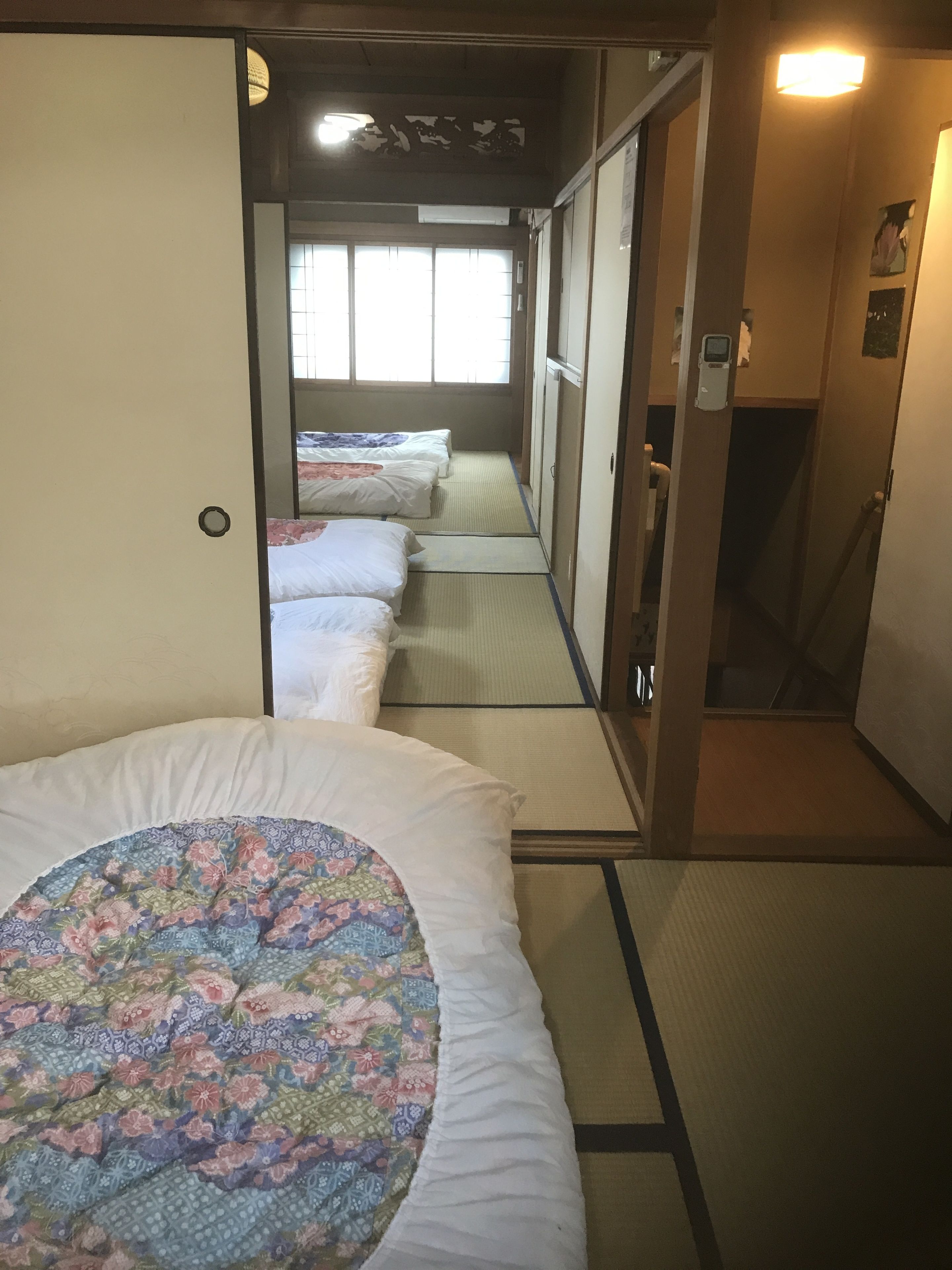A traditional Japanese-style room with tatami flooring, a futon bed with a floral-patterned blanket, and a sliding door leading to another room.