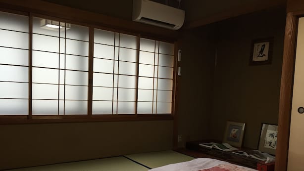 A traditional Japanese room with tatami flooring, a futon bed, shoji screens, and a small bedside table with a lamp. - Kyoto Guesthouse Oyado KEI (Kyoto)