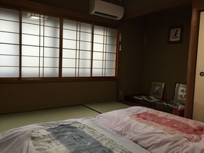Una habitación japonesa tradicional con suelo de tatami, un futón, puertas correderas shoji y una mesita de noche con lámpara.