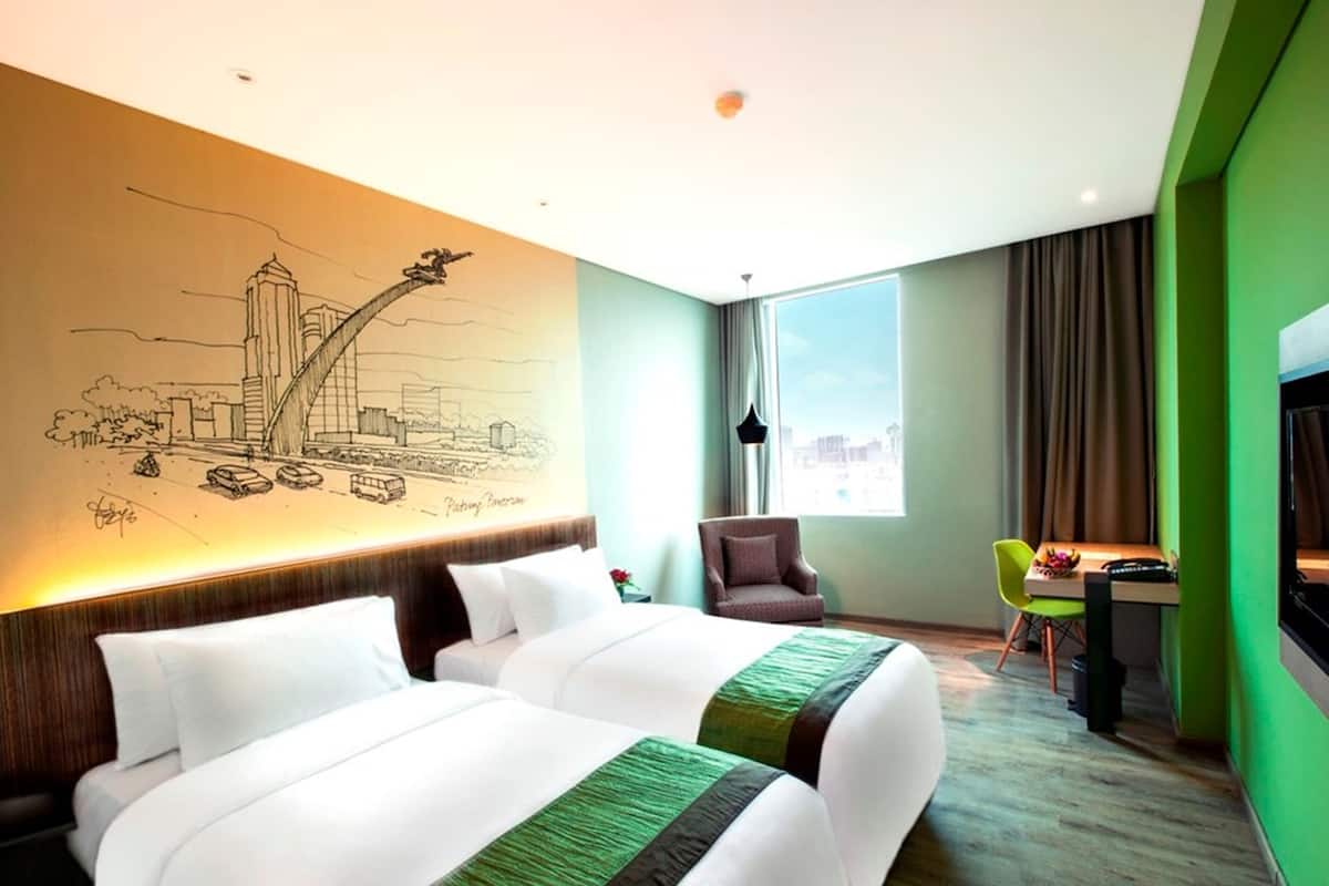 A hotel room with two beds, a desk, a chair, a large window, and a mural of a cityscape on the wall.