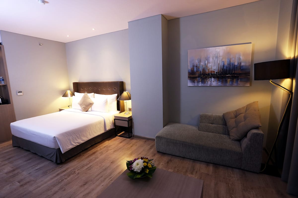 A modern hotel room with a large bed, a sofa, a painting on the wall, and a bedside table with lamps.