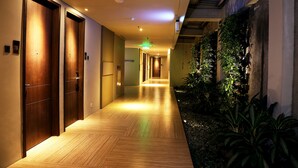 Een hotelgangen met houten deuren, een betegelde vloer en een groene wand met planten.