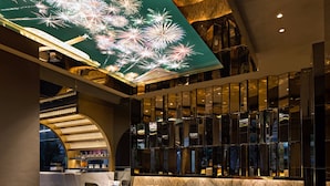 Een moderne lobby met een hoge plafond, een zithoek met banken en stoelen, een bar en een groot digitaal scherm met vuurwerk.