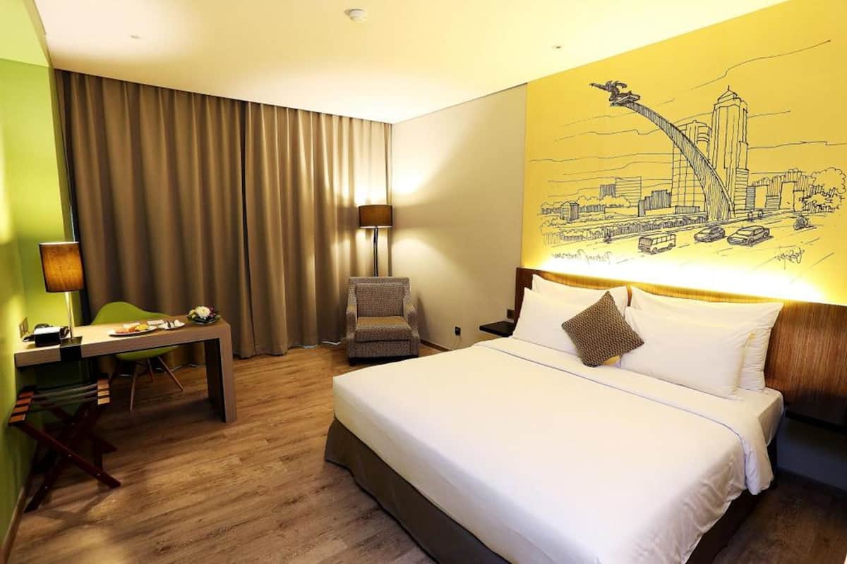 A hotel room with a bed, a desk, a chair, and a large cityscape mural on the wall.