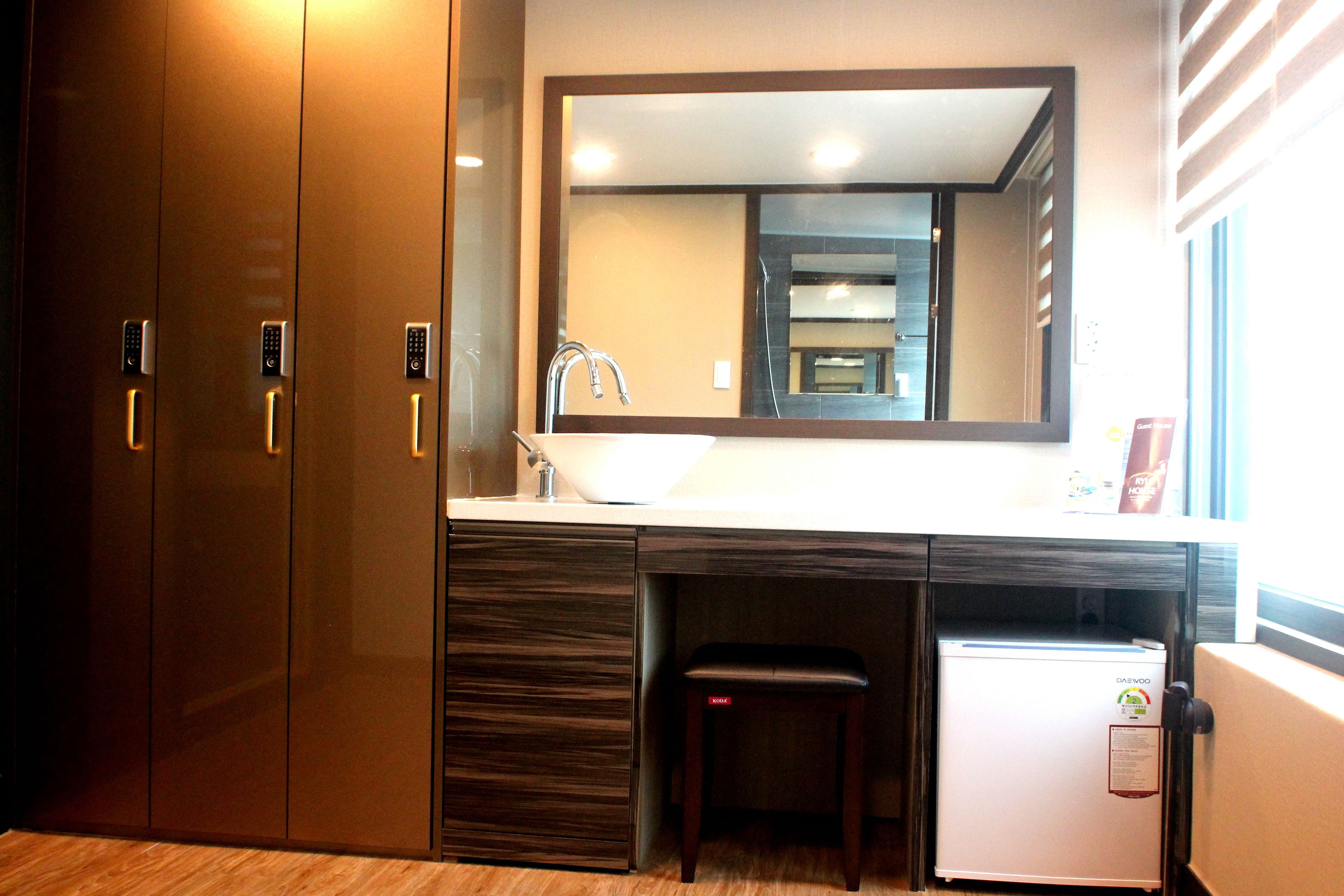 A hotel room with a wooden wardrobe, a built-in sink, a mirror, and a small refrigerator.