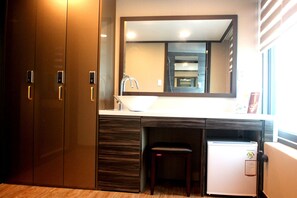 A hotel room with a wooden wardrobe, a built-in sink, a mirror, and a small refrigerator.