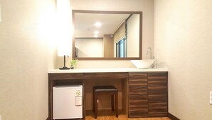 Un bagno compatto con un lavandino bianco, uno specchio sopra, un piccolo sgabello e un frigorifero bianco.