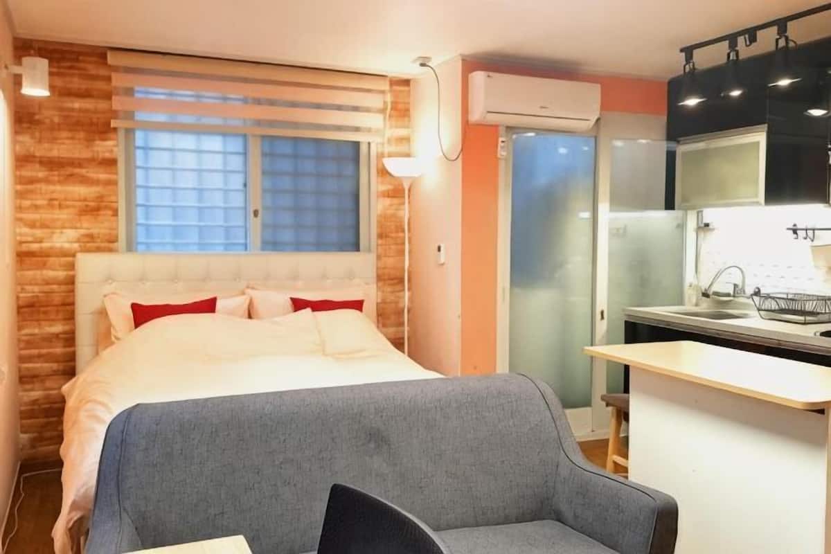 A bedroom with a bed, a desk, and a kitchenette.