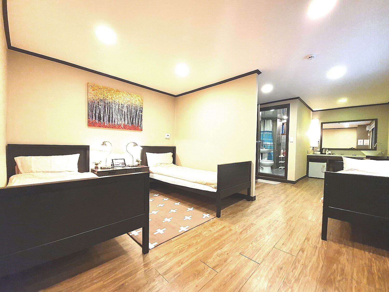 A hotel room with two beds, a desk, a chair, a bathroom visible through an open door, and a painting on the wall.