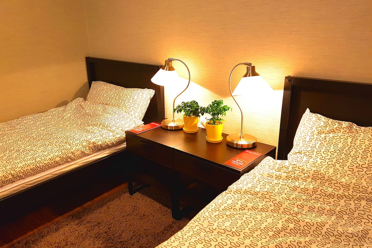 A hotel room with two single beds, a small bedside table with lamps, and a card on the table.