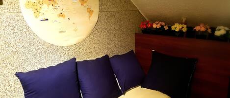 A room with a round wall map, a sofa with dark cushions, and a flower arrangement on a table.
