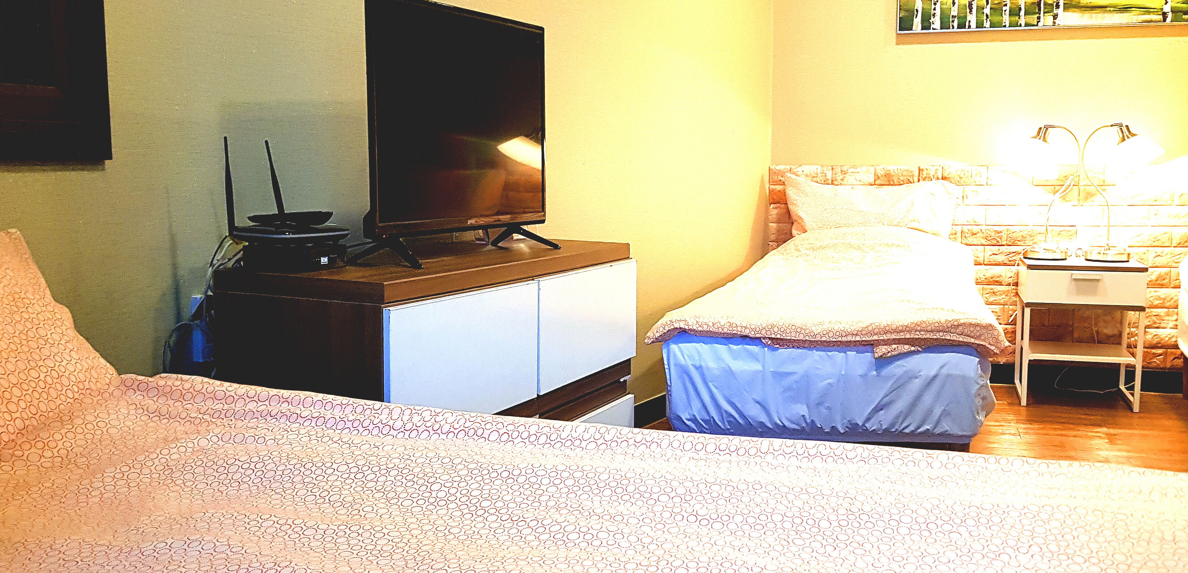 Un dormitorio con cama, televisor sobre un mueble, mesita de noche con lámparas y tocador.