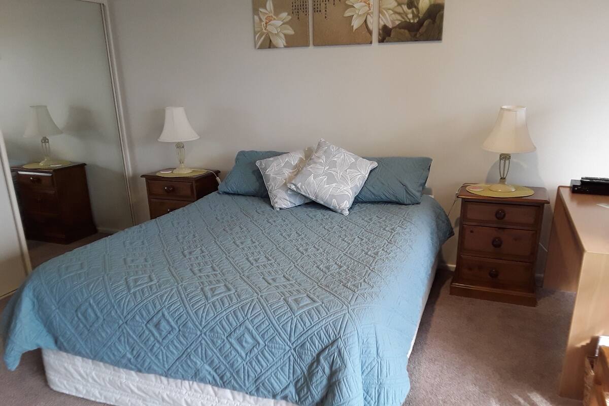 A bedroom with a bed, two nightstands, a dresser, and a mirror.