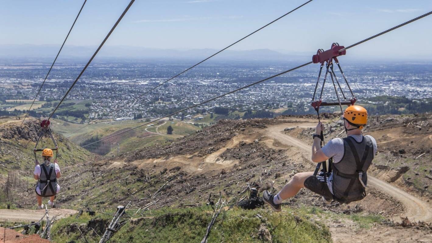 Um sistema de teleférico com passageiros, paisagem montanhosa e vista distante de uma cidade.