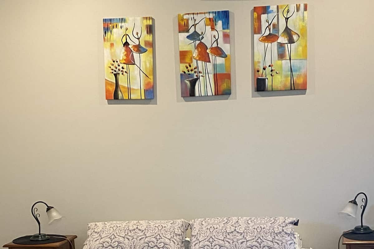 A bedroom with a bed, two nightstands, and three abstract paintings on the wall.