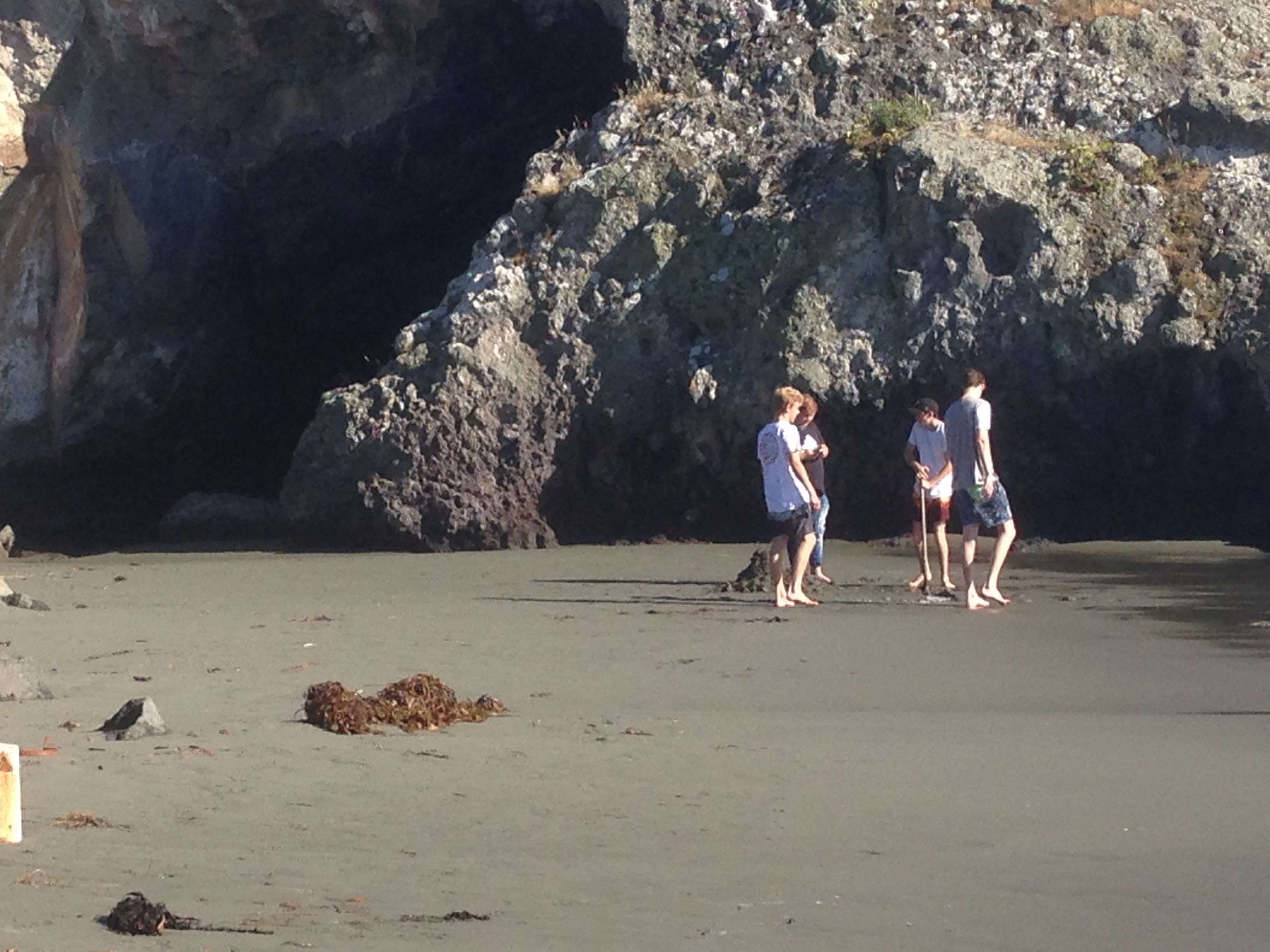 Uma praia com um penhasco rochoso ao fundo e um grupo de pessoas em pé na areia.