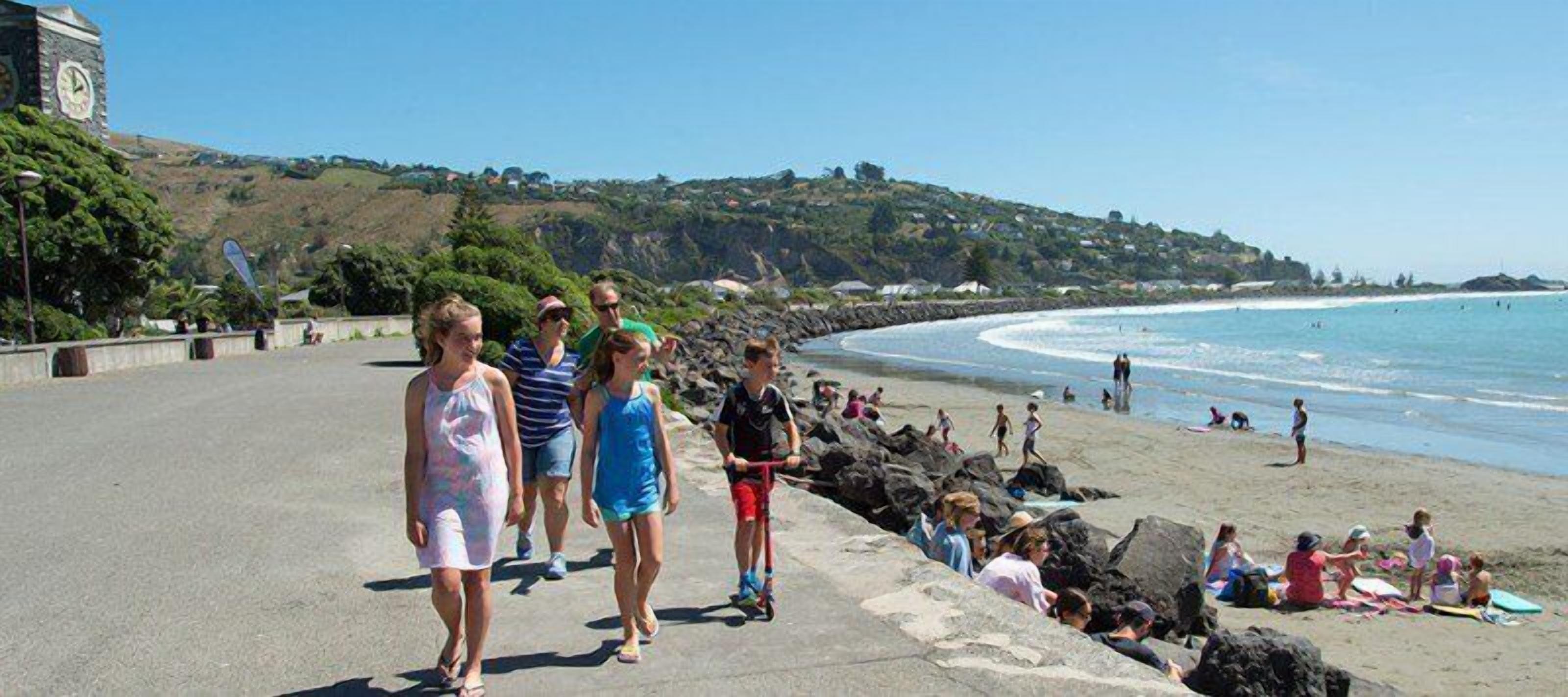 A coastal walkway with a stone wall, beach, and ocean view.