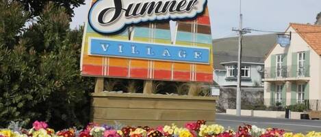 A colorful sign for 'Summer Village' with a vibrant flower bed in front.