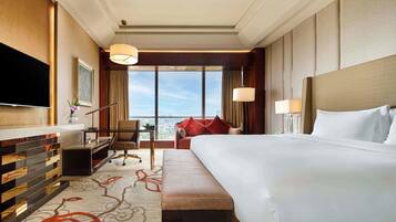 A hotel room with a large bed, a desk, a chair, a TV, and a view of the city.