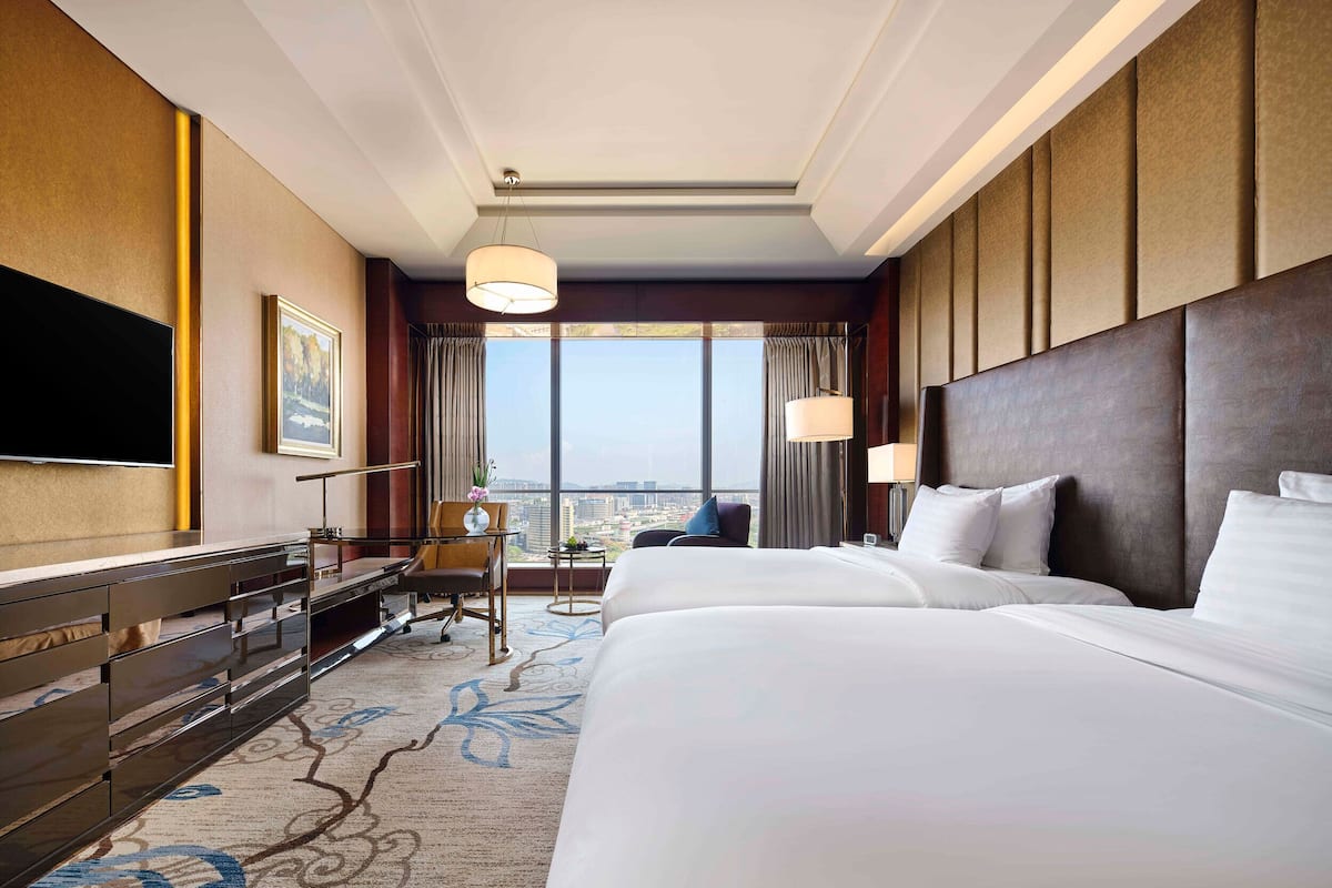 Ein Hotelzimmer mit einem großen Bett, einem Schreibtisch, einem Sessel, einem Fernseher und Blick auf die Stadt.