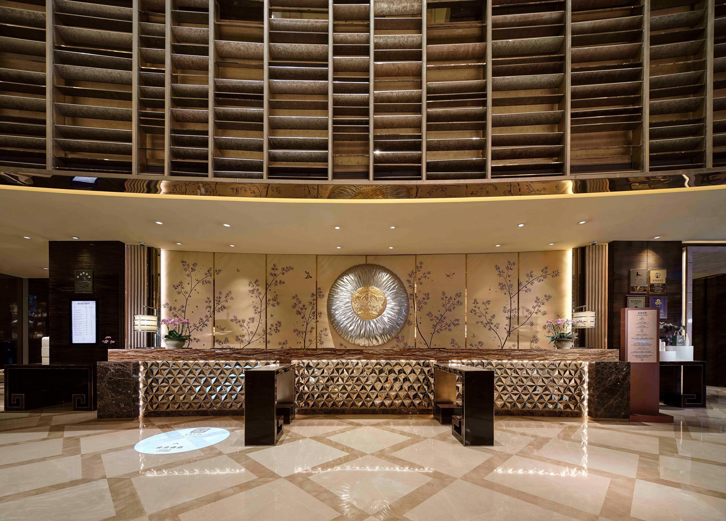Uma área de recepção com balcão de check-in, parede decorativa com design circular e parede estampada atrás do balcão.