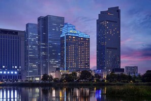 Une vue urbaine avec des immeubles modernes de grande hauteur, une étendue d’eau reflétant les bâtiments et un ciel dégagé.