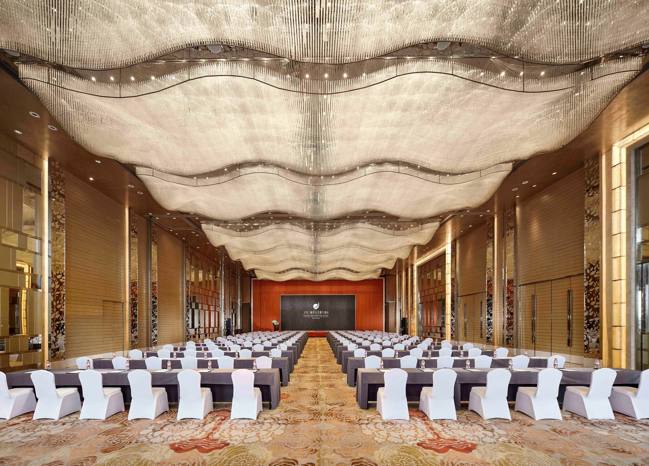 A spacious conference room with rows of tables and chairs, a patterned carpet, and a decorative ceiling.