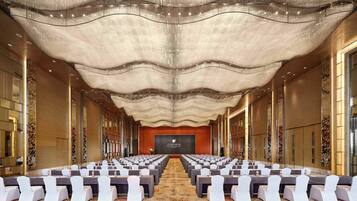 A spacious conference room with rows of tables and chairs, a patterned carpet, and a decorative ceiling.