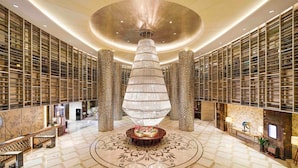 A spacious lobby with a central decorative column, a patterned floor, and bookshelves on the walls. - Sanding New Century Grand Hotel Yiwu (Jinhua)