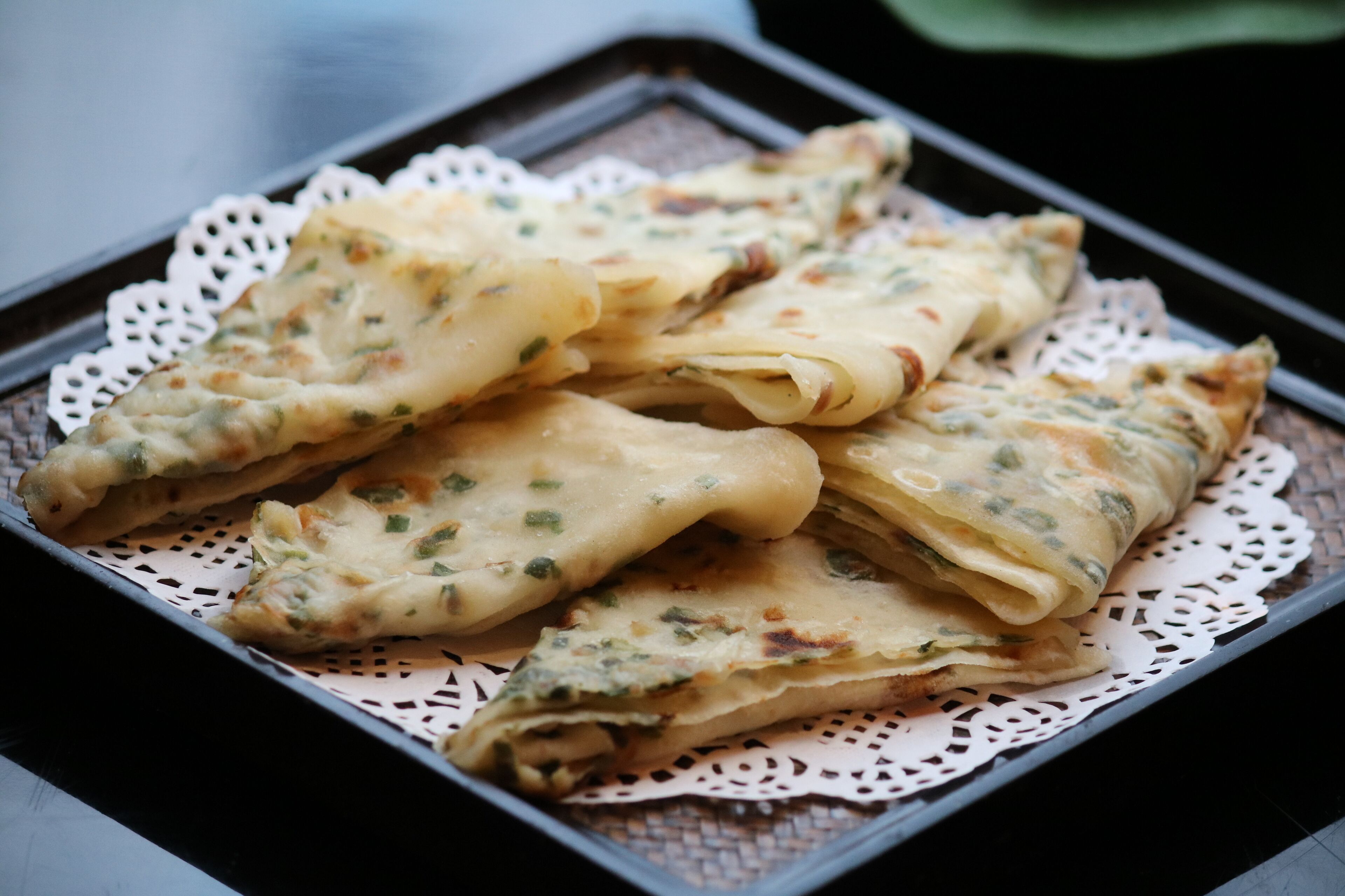 A tray of folded crepes with herbs and cheese on a lace doily.
