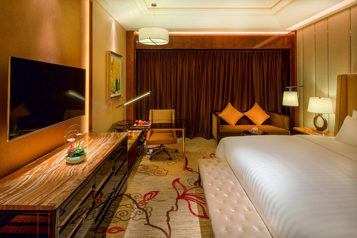 Ein Hotelzimmer mit einem großen Bett, einem Schreibtisch, einem Flachbildfernseher, einem Sessel und einer Couch mit orangefarbenen Kissen.