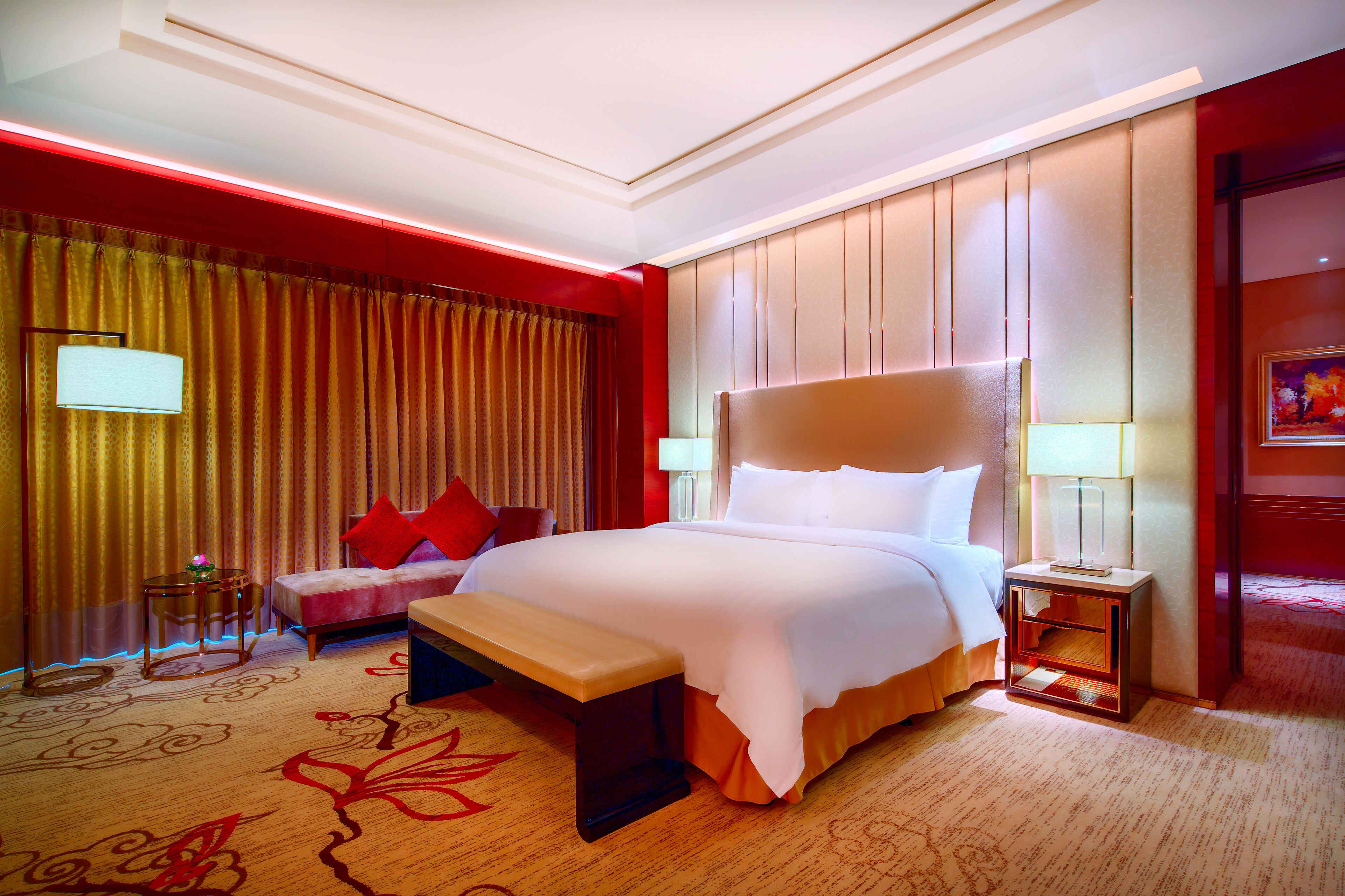 A hotel room with a large bed, a bench, a small table, and a chair.