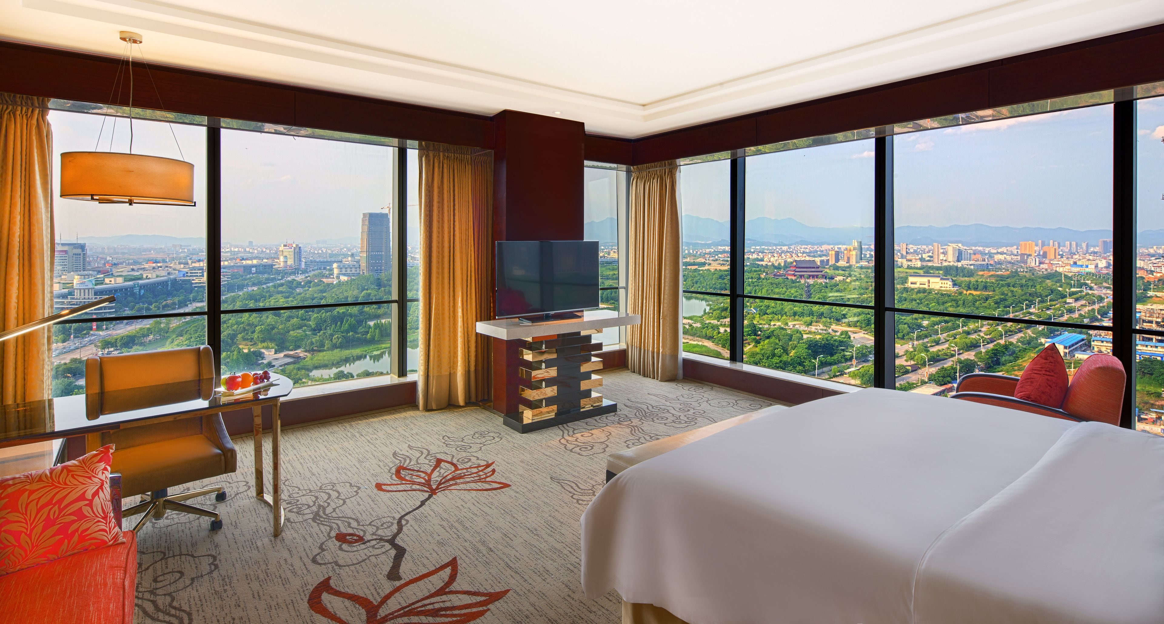 A hotel room with a large bed, a desk with a TV, and a view of a cityscape.