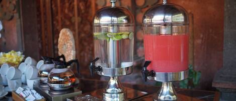 Two stainless steel beverage dispensers with transparent lids, one containing a green beverage and the other a red beverage, on a marble countertop.