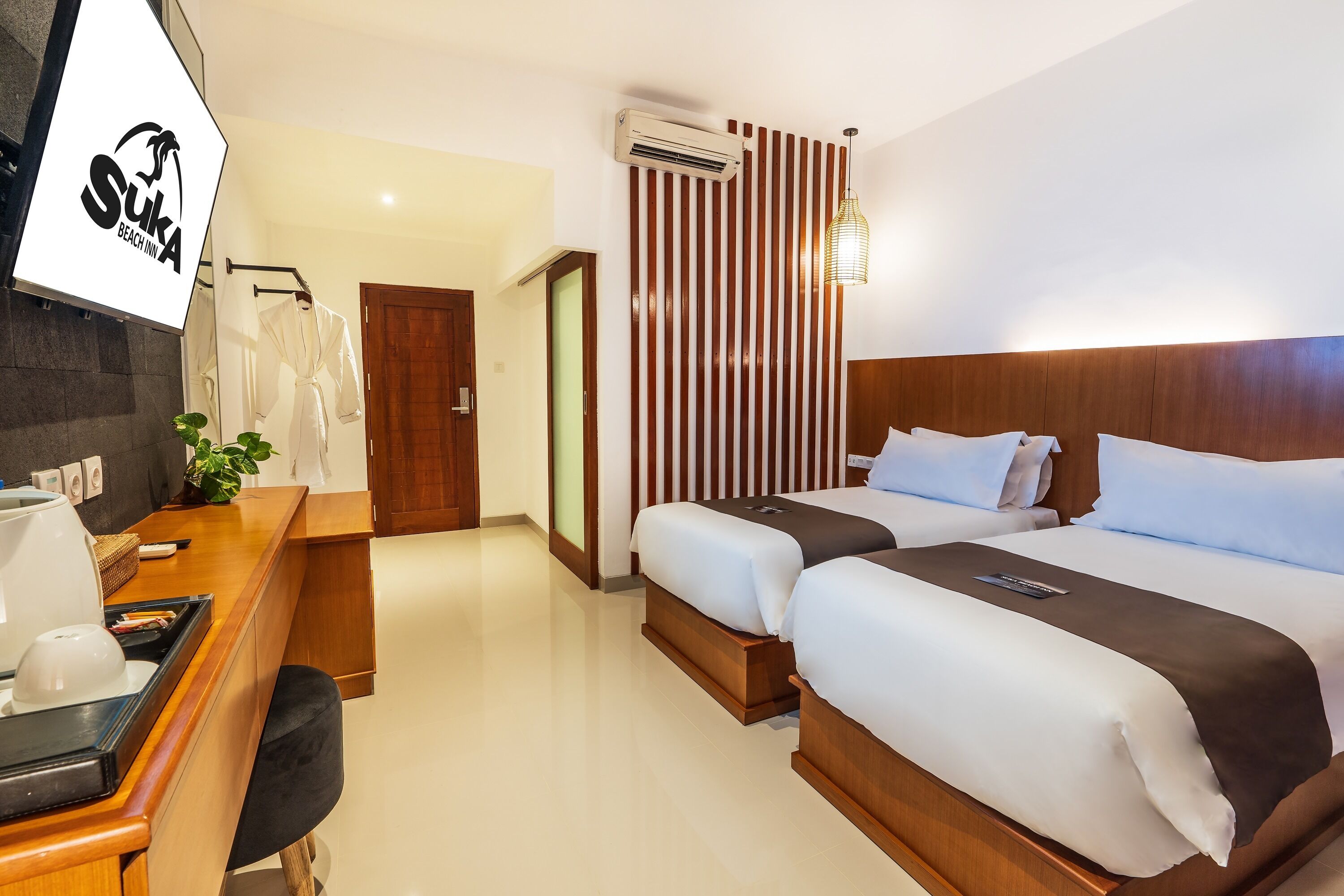 A hotel room with two beds, a desk, a chair, a TV, and an air conditioning unit.