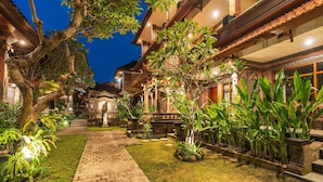 A courtyard with a brick pathway, lush greenery, and traditional architecture. - Suka Beach Inn (Kuta)