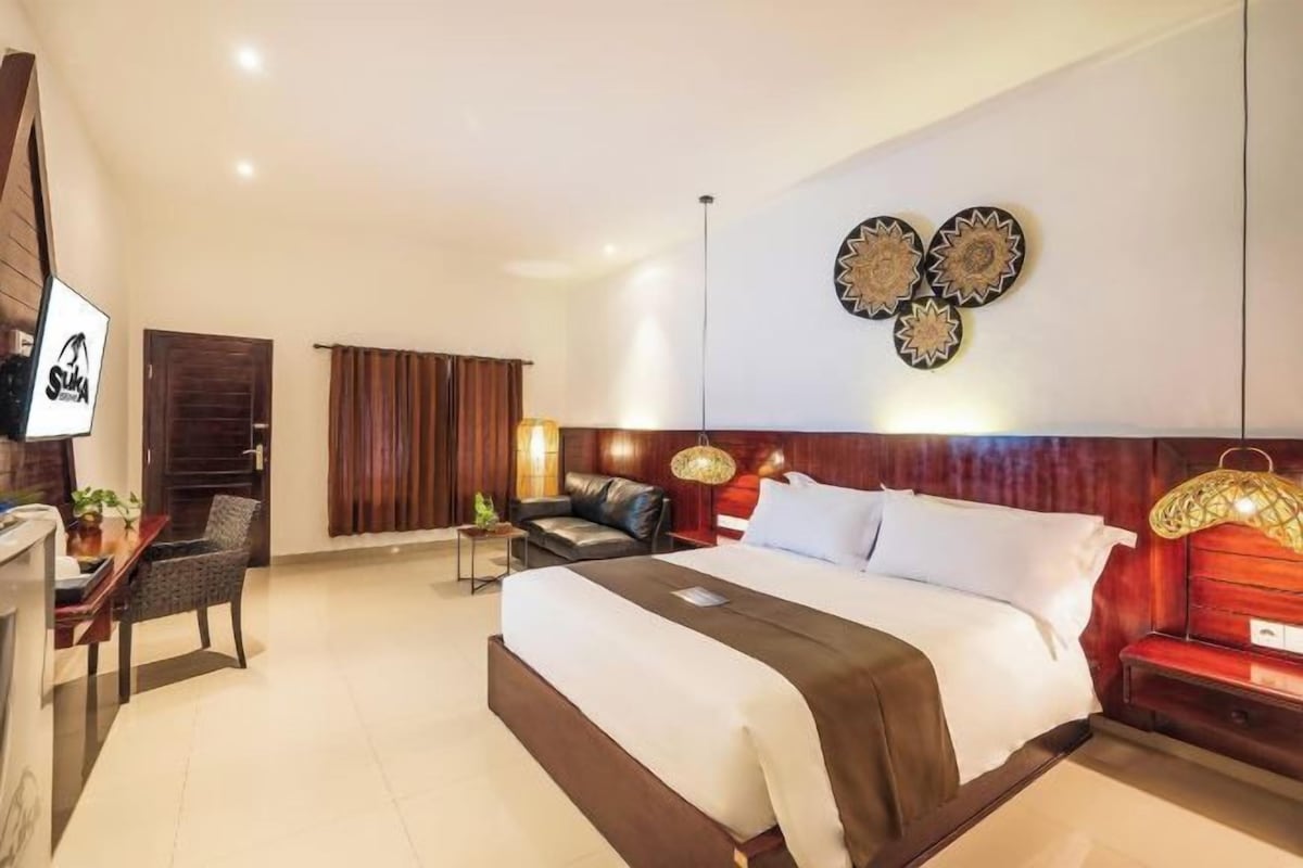 A hotel room with a large bed, a desk with a chair, a sofa, and a wall-mounted lamp.
