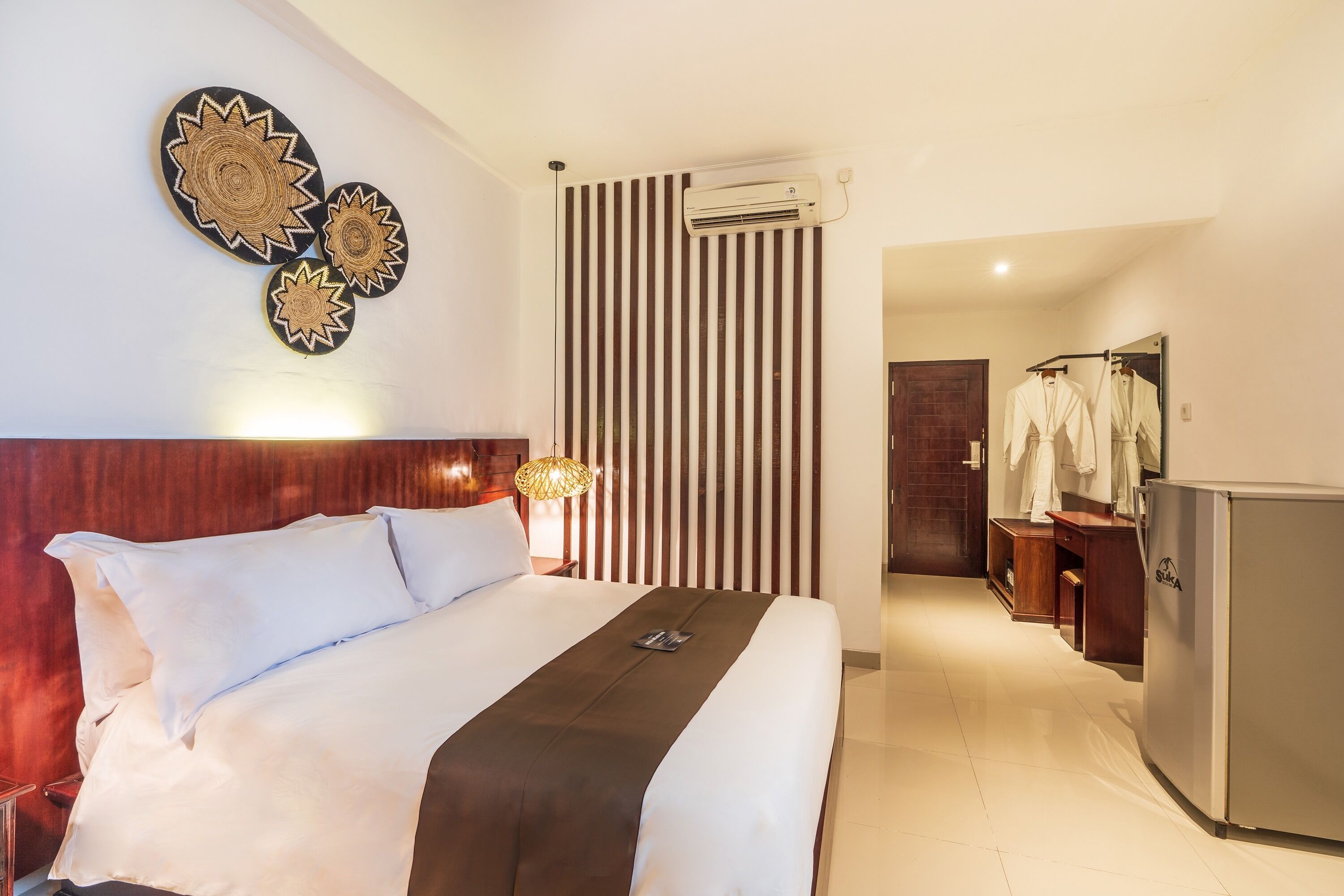 A hotel room with a bed, a wall-mounted air conditioner, a mirror, and a refrigerator.