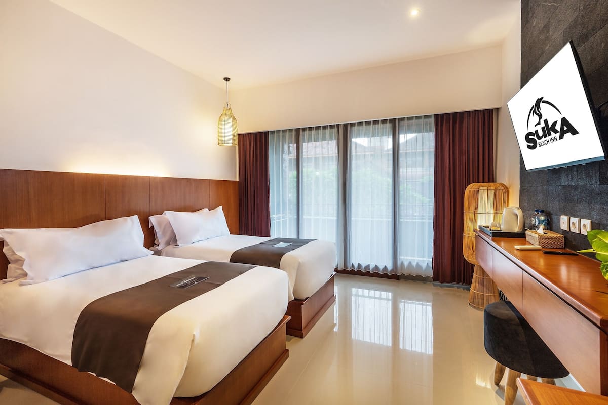 Habitación de hotel con dos camas, un escritorio, televisión y un ventanal con cortinas.