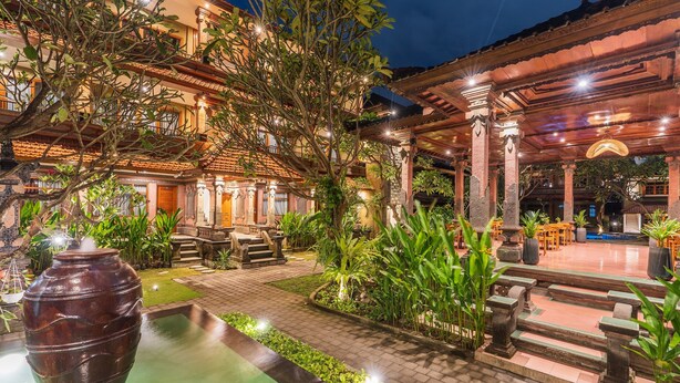 A courtyard with a large vase, stone steps, and a covered seating area with tables and chairs. - Suka Beach Inn (Kuta)