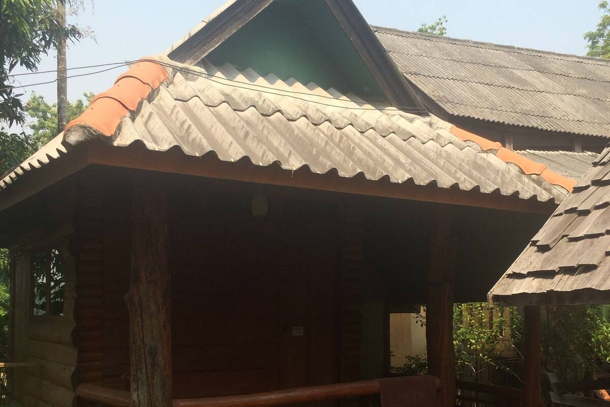 A wooden house with a tiled roof, a porch, and a small water body in front.