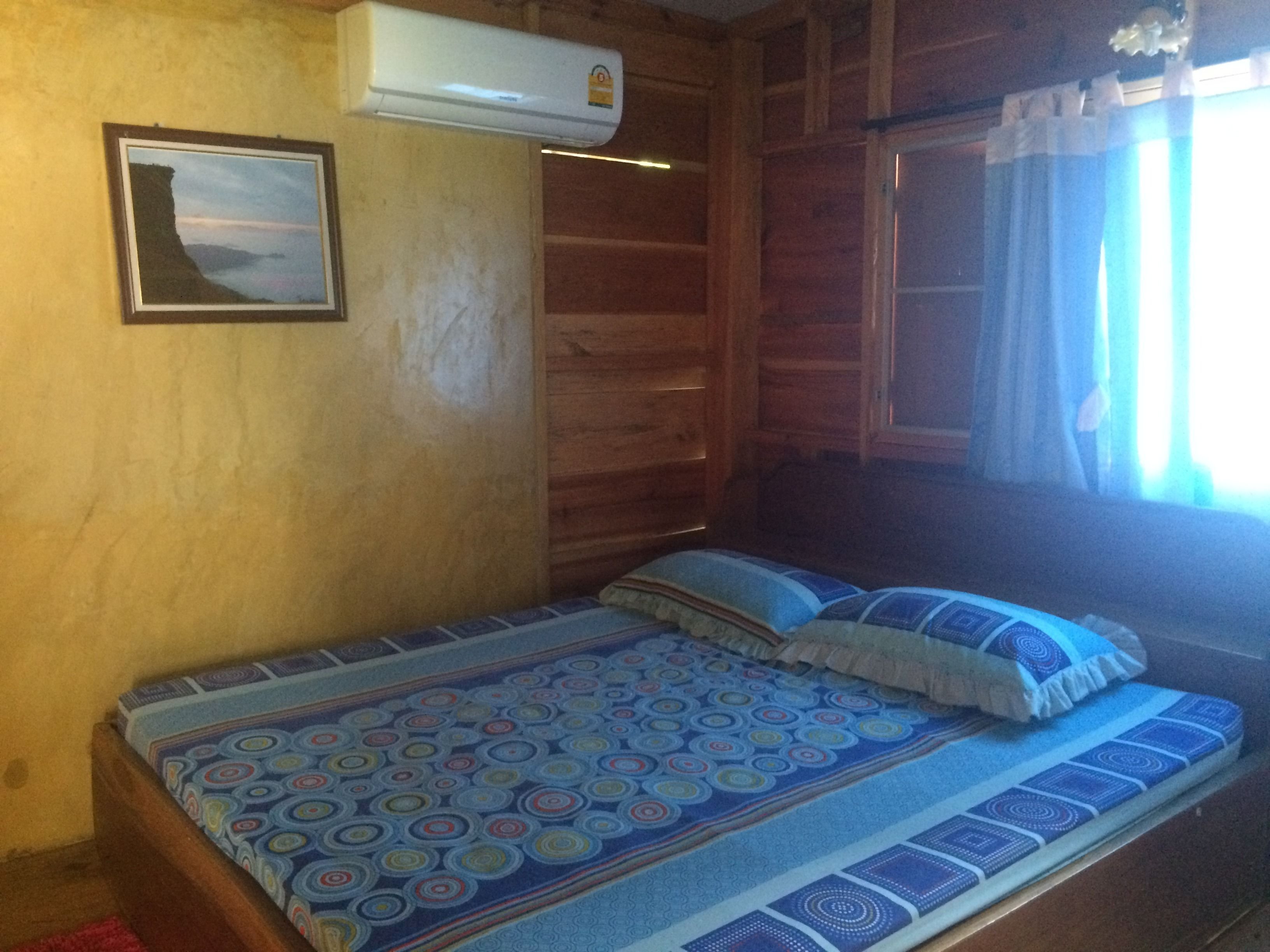 A wooden cabin room with a bed, a mounted air conditioner, and a framed picture on the wall.