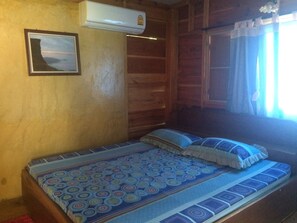A wooden cabin room with a bed, a mounted air conditioner, and a framed picture on the wall.