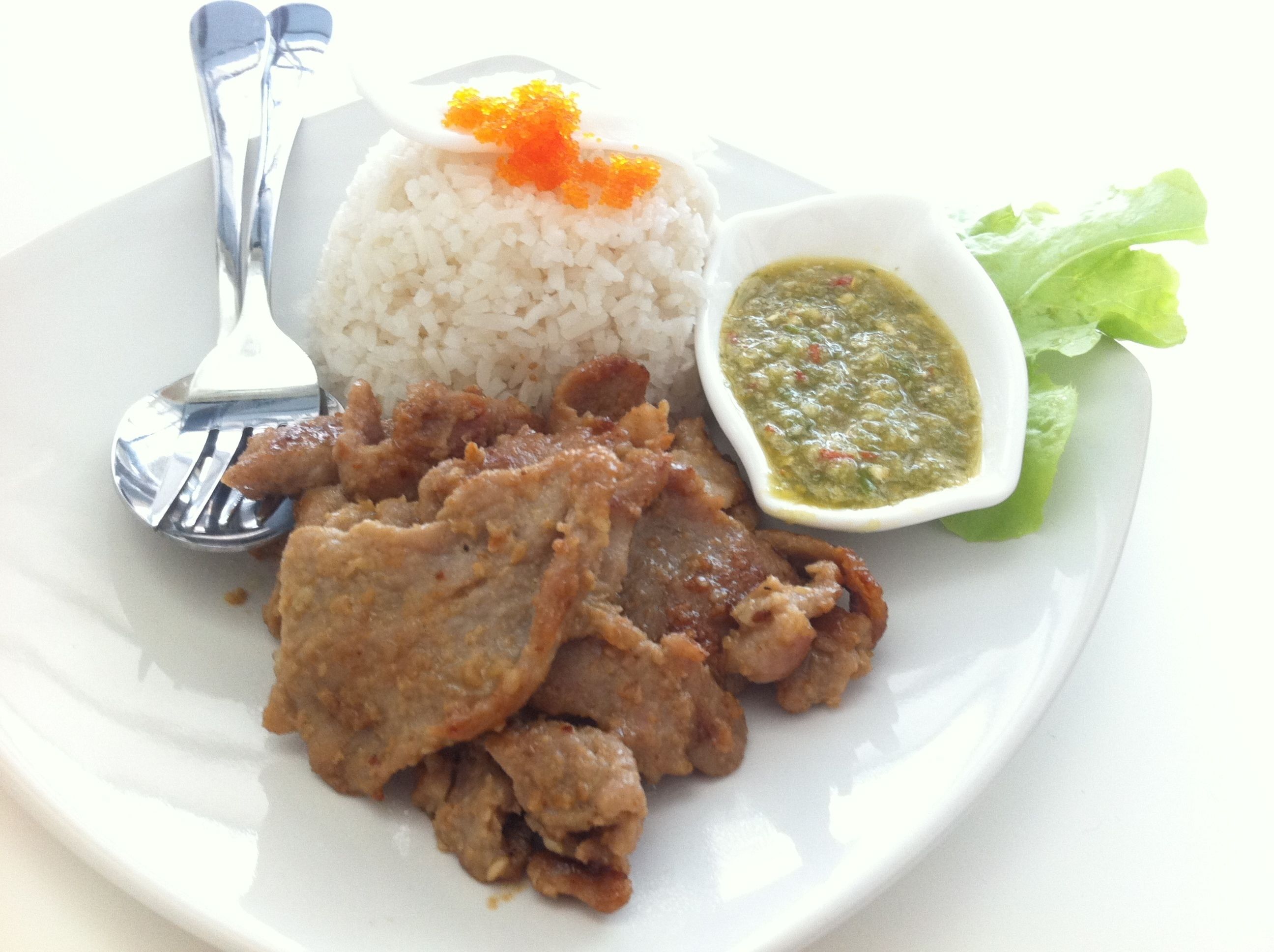 A plate with white rice, fried meat, a small bowl of green sauce, and a spoon.