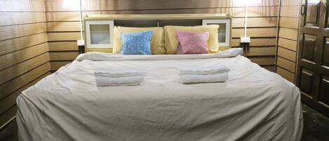 A neatly made bed with a white comforter and two folded towels, a wooden headboard, and two bedside lamps.