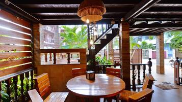 Un comedor de madera con una mesa redonda y bancos, una lámpara colgante y vistas a una escalera y follaje exterior.