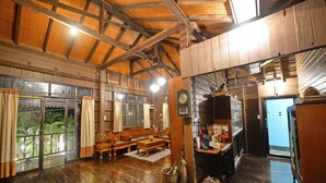 A spacious room with wooden floors, a large wooden ceiling, a wooden bench, a table, and a clock on the wall. - Huan Kawin Est.58 Lanna Home & Collection - Campus Accommodation (Chiang Rai)