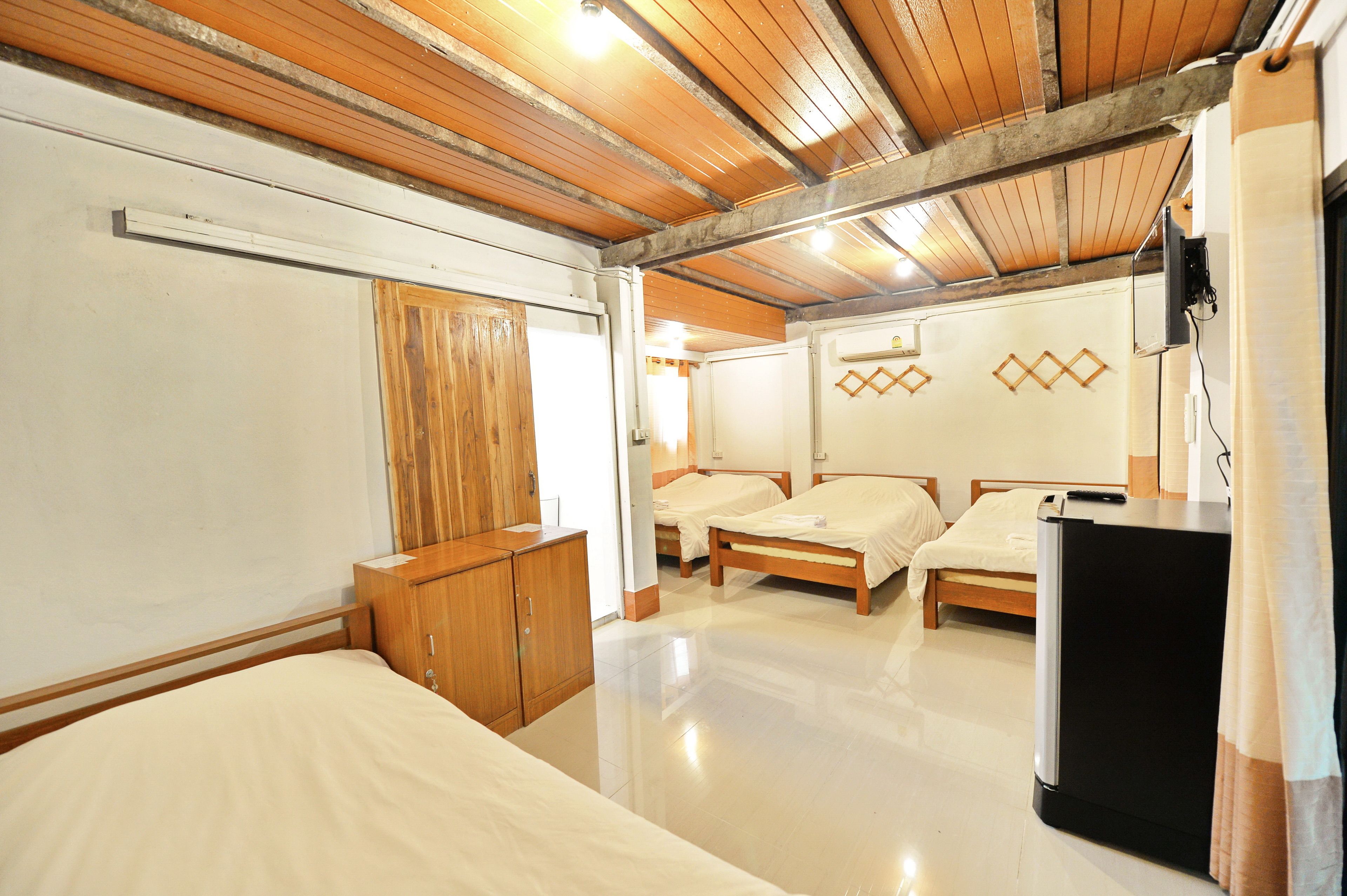 A hotel room with three single beds, wooden ceiling beams, a wooden wardrobe, a flat-screen TV, and a refrigerator.