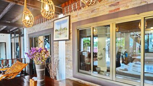 A wooden table with a vase of purple flowers, a framed picture on the wall, and a large window reflecting interior furnishings. - Huan Kawin Est.58 Lanna Home & Collection - Campus Accommodation (Chiang Rai)
